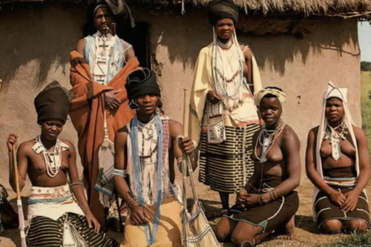 Amapondo people wearing traditional clothing outside a mud hut