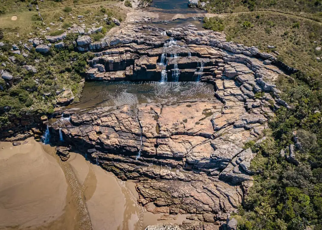 Aerial view of Mkambati Falls cascading over flat sandstone shelves into a sandy gorge, Eastern Cape