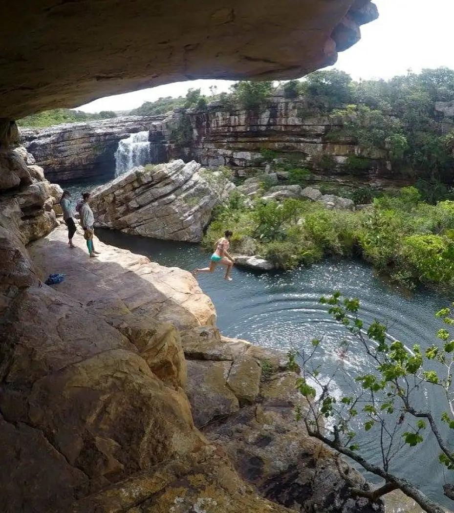 View from inside Baboon Cave overhang at Mkambathi Falls, hikers on rocks beside the natural pool below a waterfall, Wild Coast